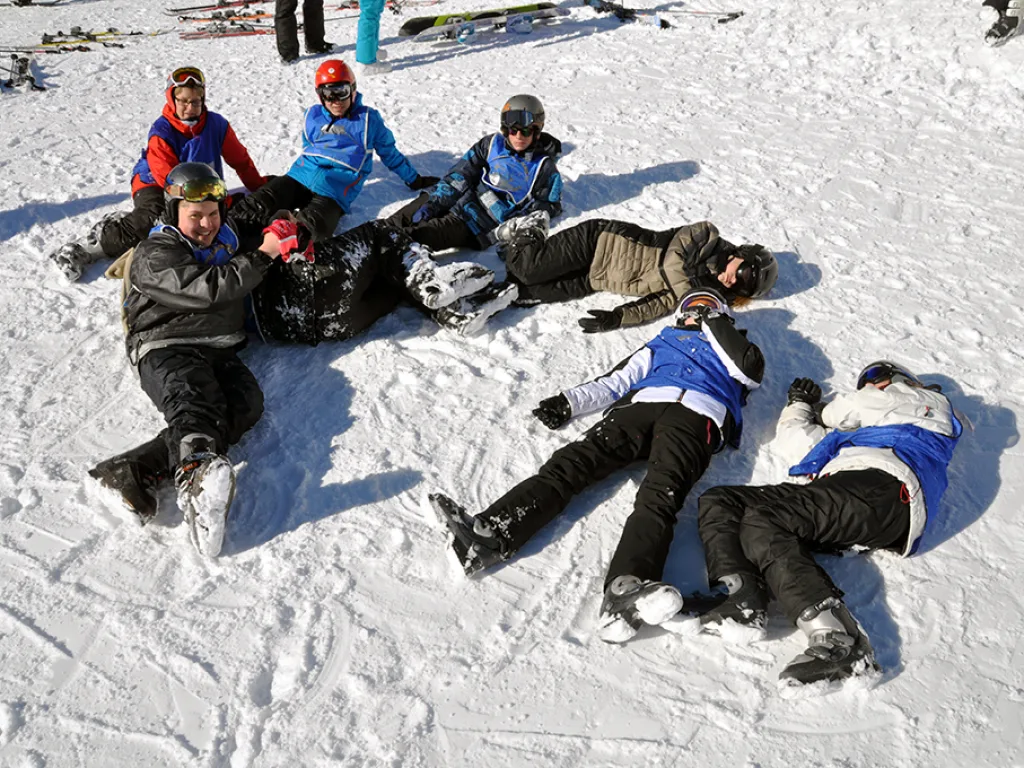 Jugendliche liegen im Schnee und lachen.